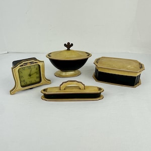 May include: A collection of vintage decorative items, including a small clock with Roman numerals, a lidded bowl, a rectangular box, and a tray. The items feature a cream and black color scheme with gold accents, suggesting a classic or antique aesthetic.
