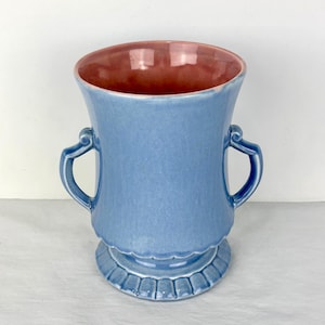 May include: A blue ceramic vase with a pink interior. The vase has two handles and a scalloped base. The vase is approximately 8 inches tall.