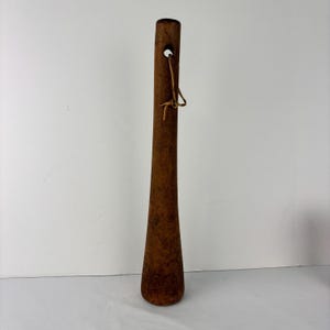 Könnte beinhalten: Ein hoher, brauner Schuhanzieher aus Holz mit konischem Design. Oben befindet sich ein kleines Loch mit einer Lederkordel. Der Schuhanzieher ist dunkelbraun und hat eine glatte, polierte Oberfläche.