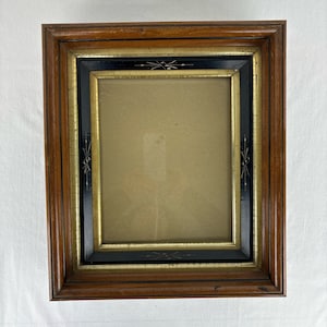 May include: A rectangular wooden picture frame with a dark brown finish. The frame has a black and gold inner border with decorative accents. The frame is empty, ready to display a photograph or artwork.