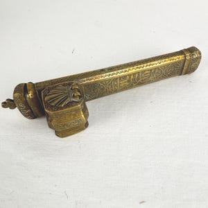 May include: An antique brass letter opener with intricate engraved patterns and Arabic script. The opener features a decorative handle and a long, slender blade. The brass has a warm, aged patina, suggesting its vintage. The overall design is ornate and detailed.