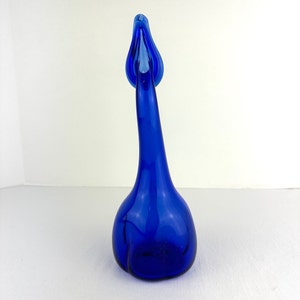 May include: A vibrant cobalt blue glass vase shaped like a swan with a long, slender neck and a rounded base. The glass is translucent and smooth, featuring a curved, elongated neck that tapers toward the top, ending in a flared, open rim.