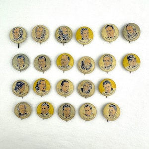 May include: A collection of twenty-three circular pinback buttons featuring black and white portraits of various historical figures and actors. Each button includes the name of the individual printed in black text below their illustrated likeness.