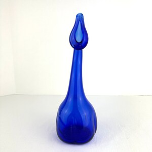 May include: A vibrant cobalt blue glass vase featuring a rounded base that tapers into a long, slender neck. The top of the vase flares out into a distinct, organic, teardrop-shaped opening, creating a smooth, continuous silhouette in translucent glass.