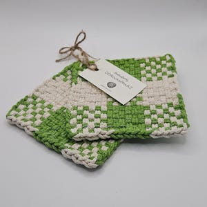 May include: Two square, woven potholders in a green and cream checkerboard pattern. The potholders are handmade and have a tag that reads "handcrafted by DDRocksPhxAZ". The potholders are tied together with twine.