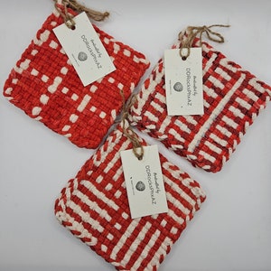 May include: Three square, woven pot holders in red and off-white. Each pot holder has a tag attached with twine. The tags read "Handcrafted by DDRocksPhxAZ" and "Made in the USA".
