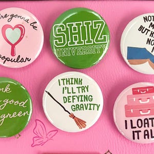 May include: Six green and white button pins with various sayings. The pins feature sayings like "you're gonna be popular", "pink goes good with green", "SHIZ UNIVERSITY", "I think I'll try defying gravity", "Nothing matters but knowing nothing matter", and "I loathe it all".
