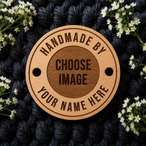 May include: A circular wooden tag featuring a light wood outer ring and a darker wood center. The text "HANDMADE BY" is engraved at the top, "CHOOSE IMAGE" in the center, and "YOUR NAME HERE" at the bottom. Two holes are on the sides.