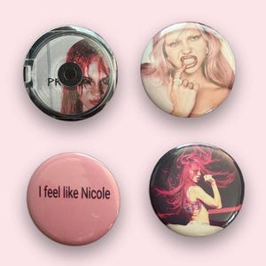 May include: Four circular pin-back buttons. One features a person with red hair, one shows a person with pink hair touching their teeth, one is solid pink with the black text I feel like Nicole, and one depicts a person with long pink hair singing.