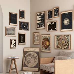 May include: A collection of framed vintage astronomical prints and illustrations, including depictions of the moon, planets, and celestial events. The artwork is displayed on a neutral wall, creating a gallery-like atmosphere. A wooden chair and side table are also visible.