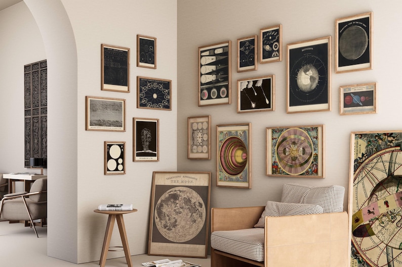 May include: A collection of framed vintage astronomical prints and illustrations, including depictions of the moon, planets, and celestial events. The artwork is displayed on a neutral wall, creating a gallery-like atmosphere. A wooden chair and side table are also visible.