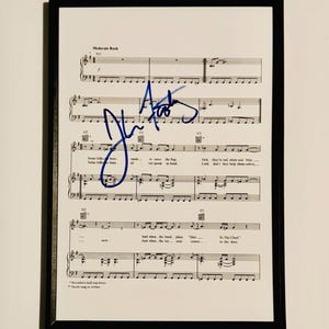May include: Framed sheet music with handwritten blue signature. The music is for a song titled "Moderate Rock." The sheet music has musical notes and lyrics. The frame is black.