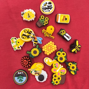 Puede incluir: Una colección de 17 abalorios para zapatos de abejas de colores amarillo, negro y coloridos. Los abalorios representan abejas, panales, girasoles y tarros de miel. Los abalorios son de goma y tienen un acabado brillante.
