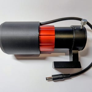 May include: A black and red cylindrical device with a black power cable and a silver adjustment screw. The device has a black base and a black cylindrical cover. The red section has a ridged design.