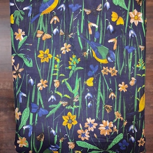 May include: A dark navy blue fabric featuring a repeating pattern of colorful birds, butterflies, and various wildflowers including yellow daffodils and blue bell-shaped flowers set against a background of tall green grass blades.