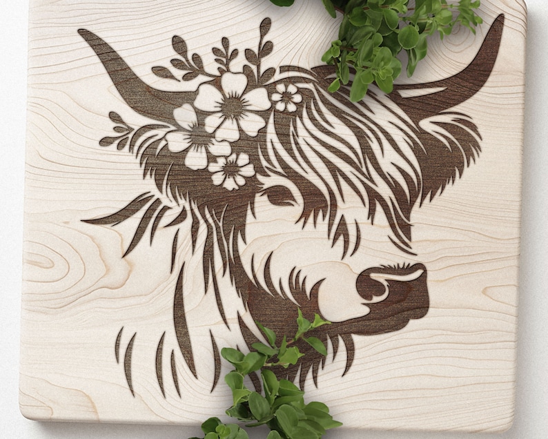 May include: A wooden cutting board with a laser-cut design of a Highland cow with a floral crown. The cow is facing to the right and has a detailed, stylized design.