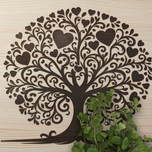 Puede incluir: Un árbol de la vida de madera marrón con una planta verde frondosa en la base. El árbol está tallado intrincadamente con un diseño de espiral y corazones.