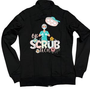 May include: Black zip-up jacket with a colorful graphic on the back. The graphic features a medical professional, flowers, and the words "OB Scrub Tech". The design includes a surgical light and the medical professional is wearing a mask.