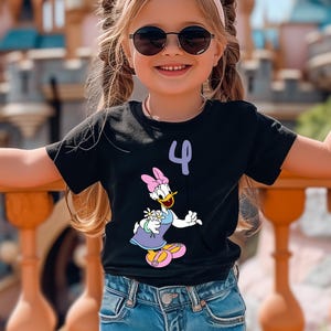 May include: Black t-shirt featuring a Daisy Duck graphic and the number 4 in purple. Daisy Duck is wearing a purple dress, pink bow, and yellow shoes. The shirt is worn by a young child wearing sunglasses.