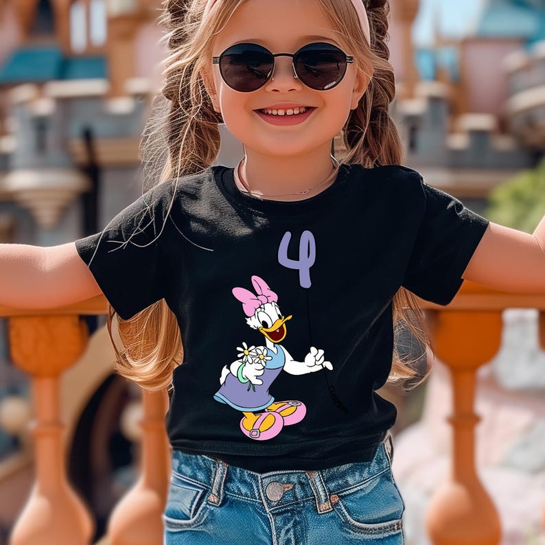 May include: Black t-shirt featuring a Daisy Duck graphic and the number 4 in purple. Daisy Duck is wearing a purple dress, pink bow, and yellow shoes. The shirt is worn by a young child wearing sunglasses.