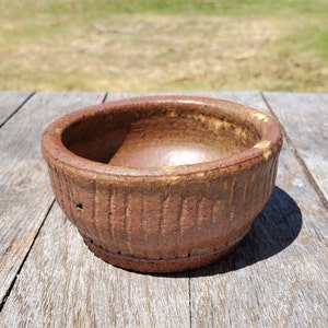 May include: A small, brown ceramic bowl with a textured, ribbed exterior. The bowl has a slightly rounded shape and a smooth, glazed interior.