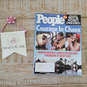 May include: A magazine with the title "People" and the headline "Courage In Chaos" is next to a small banner with the text "Frozen In Time Antiques". The magazine cover features images of people and the banner has a pink flower.