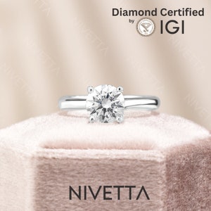 May include: A diamond engagement ring with a round brilliant cut diamond set in a white gold band. The ring is in a pink velvet box. The diamond is certified by IGI.