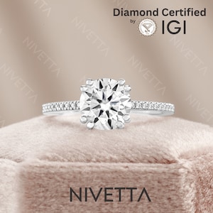 May include: A silver engagement ring with a round, clear diamond center stone and a band of smaller diamonds. The ring is in a velvet box and the words "Diamond Certified by IGI" are visible in the background.