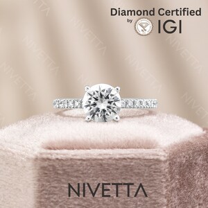 May include: A diamond engagement ring with a round brilliant cut diamond set in a white gold band. The ring is in a velvet box with the word "NIVETTA" printed on the front. The diamond is certified by IGI.