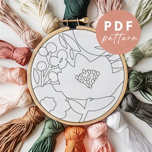 以下が含まれることがあります： 白の刺繍枠に、スタイリッシュな花と葉の黒の線画が描かれています。枠は、緑、オレンジ、ピンク、茶色など、さまざまな色の刺繍糸で囲まれています。枠の外側に、ピンクの円の中に白い文字で「PDF pattern」と書かれています。