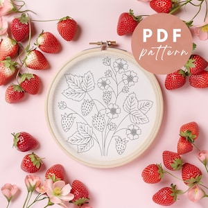 Op de afbeelding: Een witte borduurring met een zwarte lijntekening van aardbeien en bladeren. De ring is omgeven door rode aardbeien op een roze achtergrond. De tekst "PDF pattern" staat in een cirkel rechtsboven in de afbeelding.