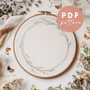 May include: A white embroidery hoop with a simple floral wreath design. The hoop is surrounded by dried flowers and butterflies.