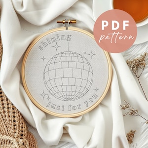 May include: A white embroidery hoop with a black and white design of a disco ball and the text "shining just for you".
