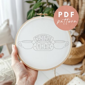 May include: White embroidery hoop featuring a black and white design of the "Central Perk" logo from the TV show "Friends". The logo includes two coffee mugs and the text "Central Perk".