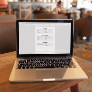 May include: A laptop computer with a white case and a black keyboard is open to a document with the title "1.2 Procurement Guide". The laptop is sitting on a wooden table.