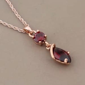 Può includere: Collana in oro rosa con due pietre rosse. Una è rotonda, l'altra a forma di marquise. La collana ha una catena delicata e un pendente dal design classico. Le pietre sono di un rosso intenso.