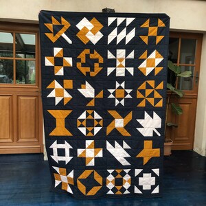 May include: A navy blue quilt with 24 different quilt blocks in white and mustard yellow. The quilt blocks are arranged in a grid pattern.