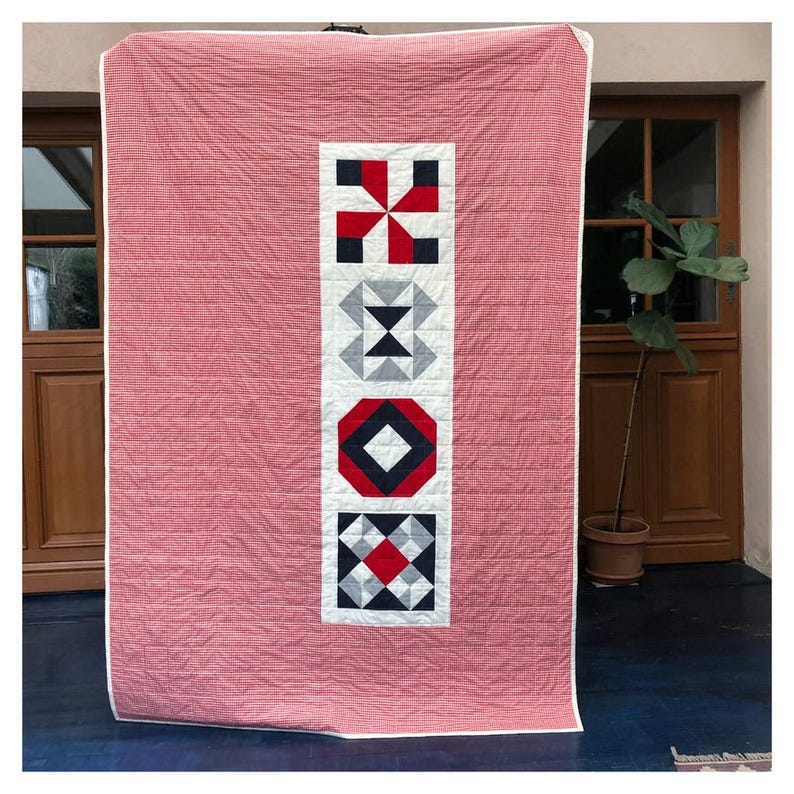 Może przedstawiać: Kołdra w kratę w kolorze czerwonym i białym z pionowym panelem pięciu r&oacute;żnych geometrycznych blok&oacute;w patchworkowych w kolorze czarnym, białym, czerwonym i szarym.