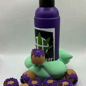 May include: A purple torch with a brown and purple cap, sitting on a green base. There are 11 brown and purple caps scattered around the base.