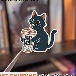 May include: A black cat sticker or car magnet drinking from a cup that says "NO ICE". The cat has green eyes and a red-lined ear. The sticker is held by tweezers. The text "HannahFisherUK" is at the top.