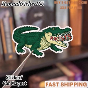 May include: A sticker or car magnet depicting a green alligator with the word "RACISTS" in red and white. The sticker has a white border. The text "HannahFisherUK" is at the top left. The text "BUY 5 GET 1 STICKER 2X2 FOR FREE" is at the top right.