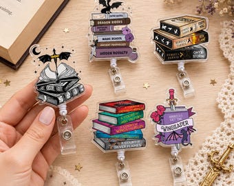 May include: Five acrylic badge reels featuring book-themed designs. One shows an open book with a sword and bat wings. Others depict stacks of books with titles like Dragon Riders, Fourth Wing, Iron Flame, Onyx Storm, and A Court of Thorns and Roses.