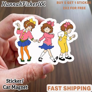 Könnte beinhalten: Ein Aufkleber oder Auto-Magnet mit drei Cartoon-Mädchen in farbenfrohen Outfits. Die Mädchen haben braune Haare und tragen rosa, blaue und gelbe Kleidung. Der Aufkleber enthält auch den Text "HannahFisherUK", "BUY 5 GET 1 STICKER", "2X2 FOR FREE", "Sticker/ Car Magnet" und "FAST SHIPPING".
