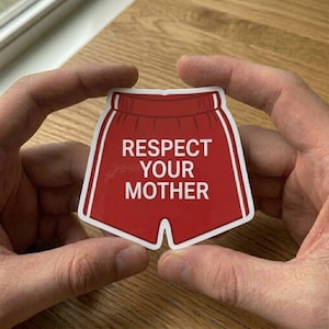 Könnte beinhalten: Ein roter Aufkleber in Form einer Boxershorts mit weißer Umrandung und dem weißen Schriftzug "RESPECT YOUR MOTHER". Der Aufkleber wird zwischen zwei Händen gehalten.