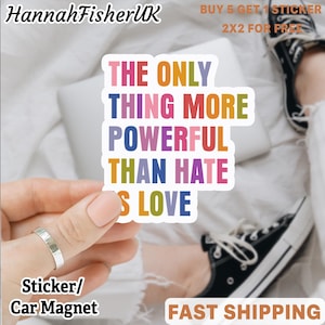 Może przedstawiać: Kolorowa naklejka lub magnes na samochód z napisem "THE ONLY THING MORE POWERFUL THAN HATE IS LOVE". Tekst jest w różnych kolorach. Produkt jest trzymany przez osobę. Nazwa marki "HannahFisherUK" znajduje się w lewym górnym rogu.