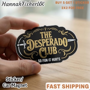 May include: A black sticker with a gold-coloured border and decorative flourishes. The text reads THE DESPERADO CLUB in a large serif font, with a sword graphic running horizontally through the centre and the phrase SO FUN IT HURTS below.