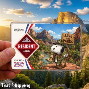 May include: A clear plastic card featuring a scenic landscape with Snoopy holding a "Save the Parks" sign. The card also displays "Resident Annual" and "America 250" text. The background shows mountains, a river, and a blue sky.