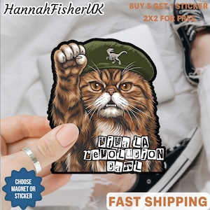 Puede incluir: Una pegatina con un gato marrón con boina verde levantando una pata. La pegatina tiene el texto "Viva La Revolucion Carl". La pegatina está sujeta por una mano. El nombre del vendedor es "HannahFisherUK".