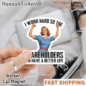 May include: A sticker or car magnet with a retro design. It shows a woman in a blue dress with the text "I WORK HARD SO THE SHAREHOLDERS HAVE A BETTER LIFE." The sticker is held by a hand with a silver ring. The brand name "HannahFisherUK" is at the top.
