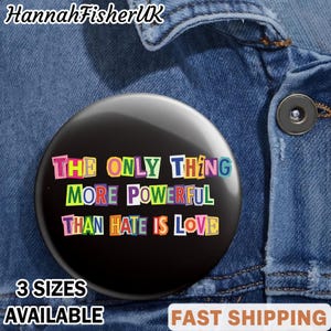 May include: A black badge with the message "THE ONLY THING MORE POWERFUL THAN HATE IS LOVE" in multi-coloured letters. The badge is set against a denim jacket. The text "3 SIZES AVAILABLE" is also visible.
